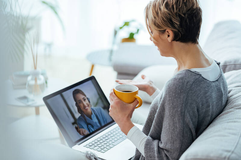 Frau sitzt gemütlich mit dem Laptop auf dem Schoß zuhause und spricht ihren Arzt online